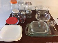 Two Pyrex glass mixing bowls, rectangular glass casseroles with lids, small glass citrus juicer, and additional glass containers with lids.