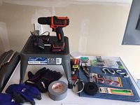 Overview of the lot showing the step stool, Black & Decker drill, gloves, duct tape, and hardware items arranged on a surface.
