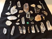Top view of multiple crystals and mineral specimens arranged on black cloth, showing clear quartz points, smoky quartz, amethyst, and various polished stones and pendants.