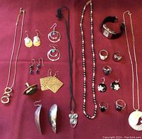 Overview of laid out jewelry items including necklaces, rings, earrings, and a wristwatch on burgundy cloth.