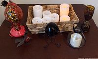 Eight LED pillar candles including one in glass and metal lantern, stained glass hummingbird feeder, metal cardinal, black glass sphere on stand, and stained glass kerosene lamp.