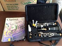 Open view of clarinet pieces laid inside the black soft carrying case beside a clarinet instructional book