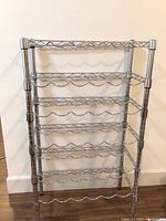 Full front view of metal wine rack showing six tiers for holding wine bottles with wave-shaped supports.