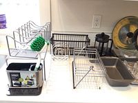 Photo showing dish soap storage with scrub brush holder, metal wire storage racks in black and white on countertop.