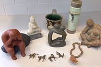 Lot items on a white surface including sculptures, Buddha, mug, candle, jewelry and figurines