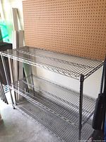 Wide view showing stainless steel wire shelving unit with three shelves and pegboard mounted behind it on wall, depicting overall size and setup.