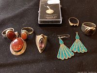 Photo showing five rings with various stones, a pair of turquoise inlay earrings, and a silver pendant in a box.