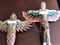 Photo showing two wooden hanging angels with painted wings and bodies, displayed on a dark surface.