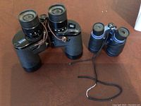 Photo of two binoculars on a brown surface, including a larger pair and a smaller pair.