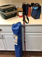 Photo showing five items on a white counter: Stanley cooler, folding chair bag, walking stick, water containers, insulated drink bag, and mug box.