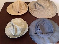 Four different women's sun hats arranged on a flat dark surface showing shapes and colors for outdoor use.