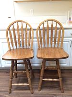 Front view of both oak wooden swiveling barstools with curved backs and four legs each.