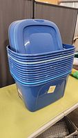 Stack of 14 blue plastic storage totes with lids, showing used condition and dust. The totes are rectangular with handles and stack neatly.