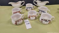 Six soup bowls with various soup names and illustrations, arranged in front of two ceramic gravy boats.
