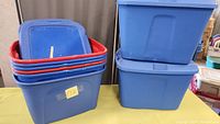 Eight blue plastic storage totes stacked, blue lids and red rims visible on some.