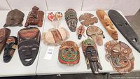 Overview of all wooden and clay masks arranged on a table showing variety of styles and sizes.