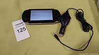 Sony PSP handheld console with lit power indicator on screen showing initial date/time setup, and lighter power cord.