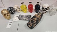 Full view of skull decorations including glass bottles with colored liquids, skull figurines, ceramic tray, and coffin box.