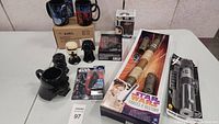 Full view of the Star Wars collectibles lot showing mugs, boxed saber replicas, figures, and other items.