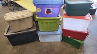Stacked variety of used plastic storage totes in various colors and sizes on warehouse floor.