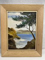 Framed oil painting on board showing coastal landscape with cliffs, tree, sailboat, and distant hills.