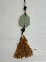 Full view of jade medallion hanging from a brown rope finished with a tassel.