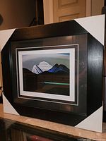 Front angle showing the entire framed print with black contemporary frame and white corner protectors.