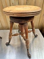 Full view of antique wooden piano stool showing round seat and turned legs ending in cast iron sea serpent feet