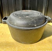 Cast iron Dutch oven pot with lid in place, showing exterior wear and cast handles.