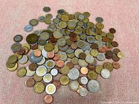 Top view showing a large pile of mixed coins from various countries, including bi-metallic and copper coins.