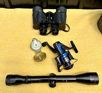 Photo showing all four items: black binoculars, Bell scope with visible wear, engineer's compass open, and blue fishing reel.