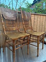 Pair of wooden pressback chairs standing outdoors showing carved high backs, turned legs and spindles, and contoured seats.