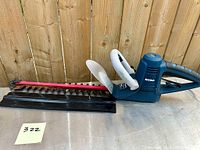 Left side view of the RONA 18-inch electric hedge trimmer with blade cover, showing the blue body, black grip handle, cord, and red/black blade guard.