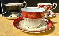 Photo showing three vintage fine bone china teacups and saucers in red, black, and floral designs