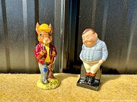 Photo of both Royal Doulton figurines, 'Autumn Days' Bunnykins rabbit and Fat Boy man, showing front views with colors and details.