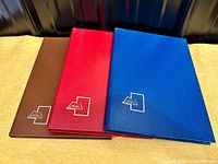 Three Philatex albums with brown, red, and blue textured covers laid flat on a surface.