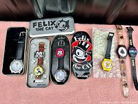 Seven vintage character and promotional wristwatches, some in original branded metal boxes, displayed on pink fabric.