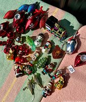 Overall layout of vintage glass Christmas ornaments including various figurines and baubles on fabric background.