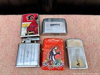 Top view of five refillable lighters arranged side by side on carpet surface showing different brands and designs