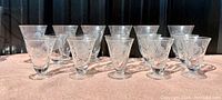 Set of 15 etched crystal glasses arranged on a pink cloth, showing varying sizes and the cornflower floral etching