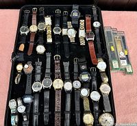Full view of all 22 wristwatches neatly organized in black zippered storage case, additional packaged watch bands at right