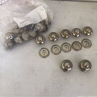Lot of silver metal cabinet knobs and matching backplates displayed on surface. Bag of extra knobs visible.