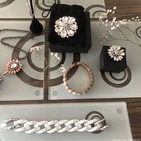 Overview of fashion jewelry items including brooches, bracelets, and part of the necklace on a patterned glass table.