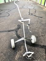 Photo of the golf cart showing the handle, strap, and wheels on asphalt ground.