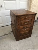 Side angle showing the oak wood construction, two drawers, metal handles, and keyholes.