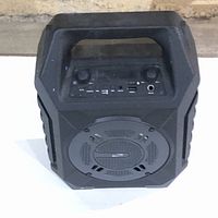 Front view of black portable speaker showing control panel with knobs and input ports under a protective clear panel.