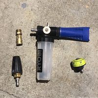 Four pressure washer accessories laid out on concrete: Ryobi foam sprayer, turbo nozzle, 5-in-1 tip, and close range adapter