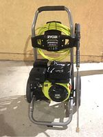 Front view of Ryobi pressure washer with coiled yellow hose and mounted spray wand