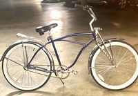 Side view of blue Schwinn 3 speed beach cruiser bicycle with whitewall tires and chrome fenders in indoor parking area.