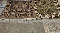 Two area rugs side-by-side on concrete floor, one with dark floral medallion and the other green floral.